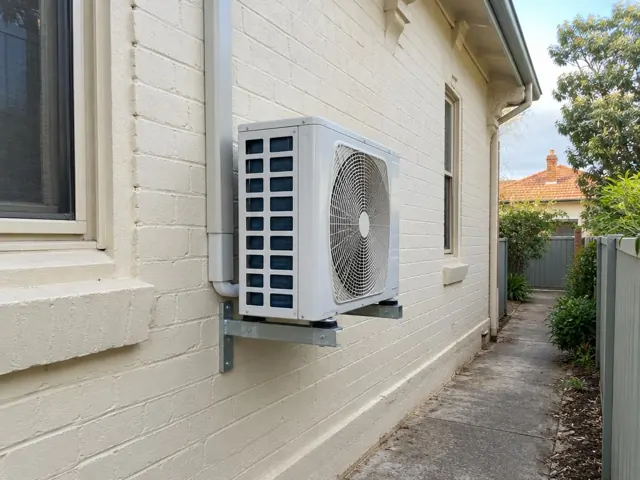 Wall-mounted outdoor air conditioner unit on a brick home exterior beside a narrow side path in Parkside